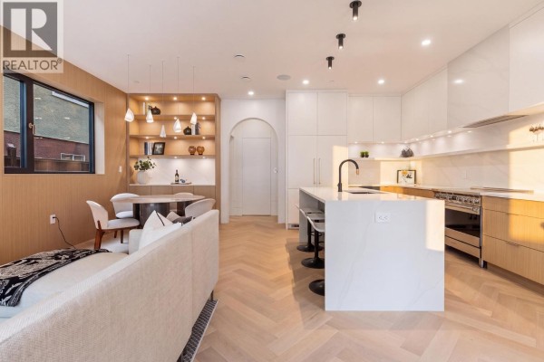 Open-concept living, dining, and kitchen area with a white island, light wood cabinets, and herringbone floors. - 2 4956 Chester Street, Vancouver