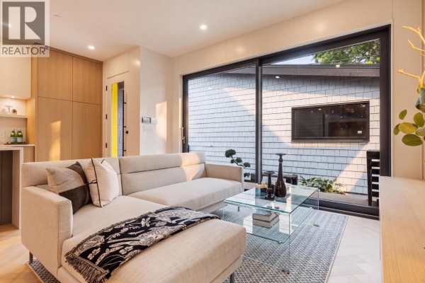 Living room with a light grey sectional sofa facing a large sliding glass door with exterior view. - 2 4956 Chester Street, Vancouver