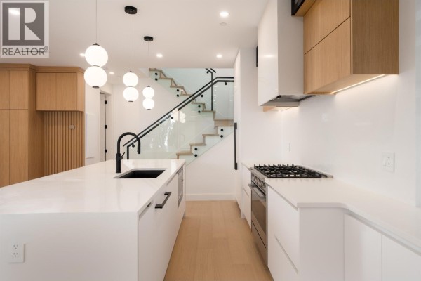 Kitchen island with sink and modern cabinetry, facing the dining area and stairs. - 2 5963 Granville Street, Vancouver