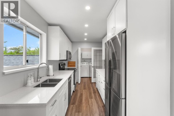 Galley kitchen with white cabinets, quartz countertops, stainless steel sink, and a laundry room at the end of the hall. - 2 6320 48a Avenue, Delta