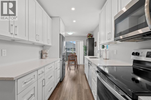 Close-up of the kitchen with white cabinets, stainless steel microwave, and stovetop with an oven below. - 2 6320 48a Avenue, Delta