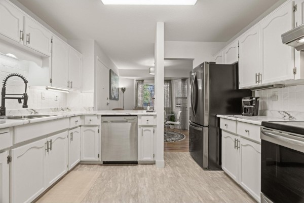 White kitchen with stainless steel appliances, granite countertops, and a view into the living area. - 2 7455 Huron Street, Sardis West Vedder, Chilliwack