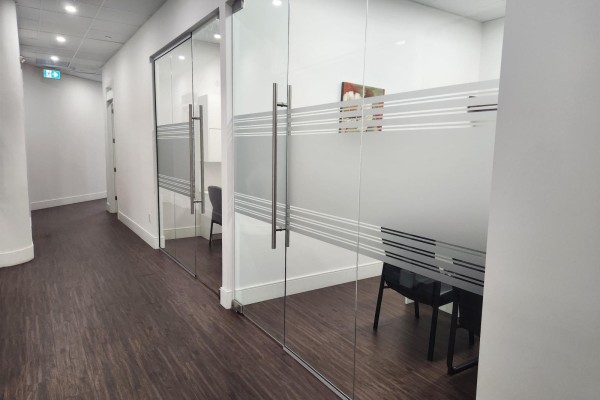 Office hallway with glass-walled offices showing interior seating and dark wood flooring. - 2 9015 120 Street, Delta