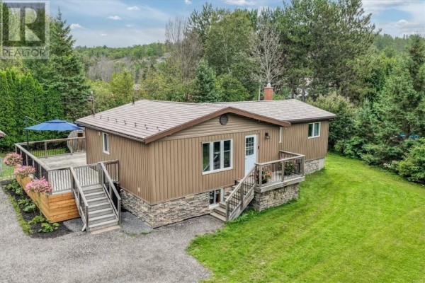 Front exterior of a brown bungalow with stone accents, a white door, and a wooden deck with stairs. - 2 Adam, Lively
