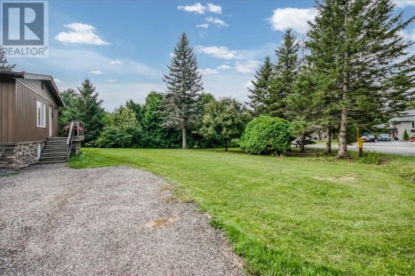 Home with gravel driveway, steps, and deck, surrounded by trees and lawn - 2 Adam Lively