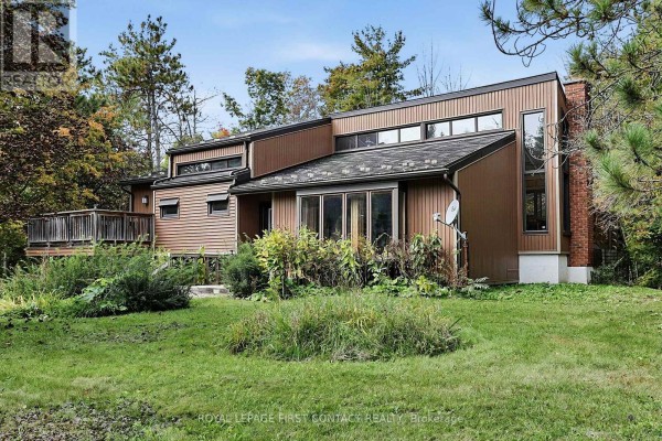 Side view of the house showcasing brown siding, large windows, and surrounding trees. - 2 Briarwood Court, Springwater
