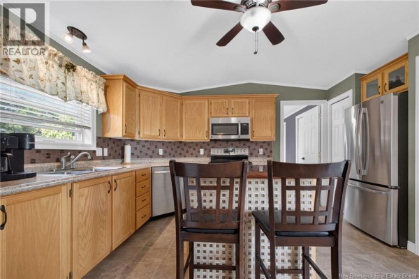 Kitchen with light wood cabinets, stainless steel appliances, a breakfast bar with stools, and tiled flooring. - 2 Bur Oak Street, Moncton