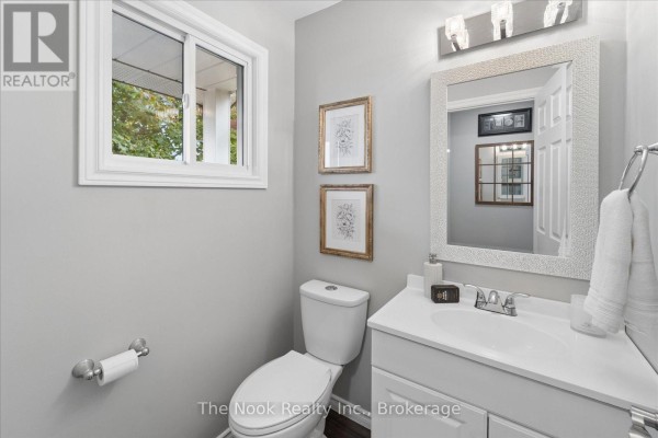 Powder room with a toilet, white vanity, decorative mirror, and a small window. - 2 Century Boulevard, Cavan Monaghan