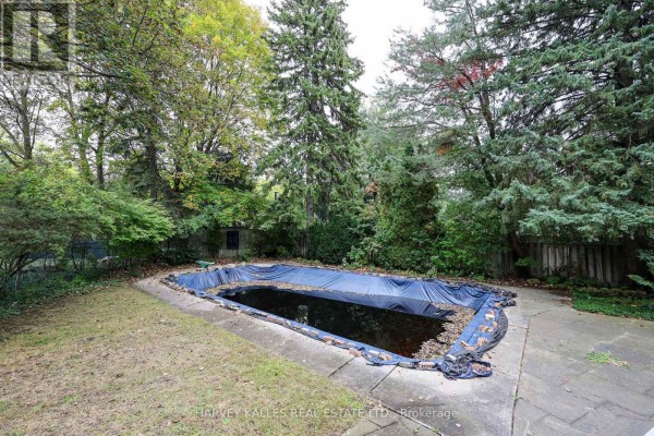 Covered outdoor swimming pool with concrete surround, surrounded by trees and grass. - 2 Clovestone Road, Toronto