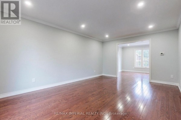 Interior view of an empty room with hardwood floors, light grey walls, and an opening to another room. - 2 Craigleith Crescent, Richmond Hill