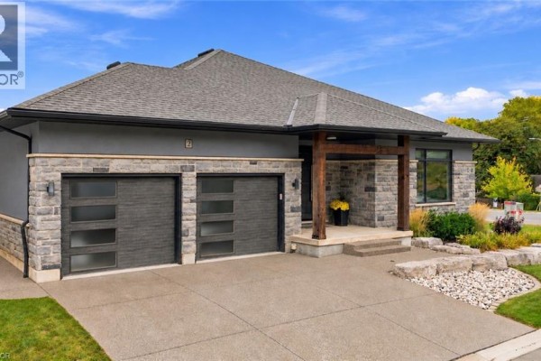 Close-up of the modern home's entrance with a covered porch, stone detailing, and a double garage with frosted glass panels. - 2 Fedorkow Lane, Niagara On The Lake