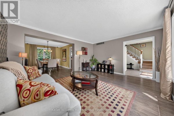 Living room with neutral walls, hardwood floors, a patterned rug, sofa, and view into dining room and stairs. - 2 Gow Street, Centre Wellington