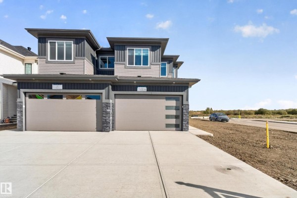 Front exterior of a duplex with grey and tan siding, double garage doors, and a car on the street. - 2 Parker Ln, Spruce Grove