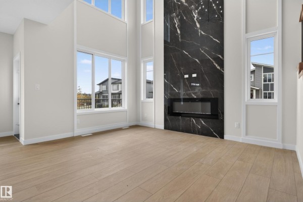 Empty living room with high ceilings, large windows, and a floor-to-ceiling black marble fireplace. - 2 Pebble Cv, Spruce Grove