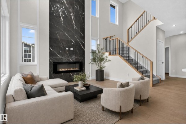 Living room with a sectional sofa, two armchairs, a large black marble fireplace, and a staircase. - 2 Pebble Cv, Spruce Grove