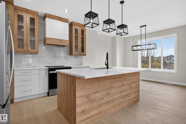 Modern kitchen with white quartz countertops, wood-look cabinets, an island, and stainless steel appliances. - 2 Pebble Cv, Spruce Grove