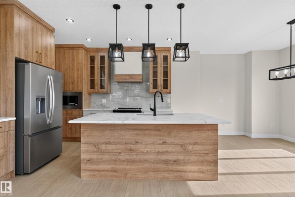 Kitchen with stainless steel refrigerator, wood-look cabinets, white countertops, and a large island. - 2 Pebble Cv, Spruce Grove