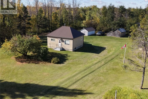 Close-up view of a beige house with a brown metal roof, adjacent to a garage and wooden shed. - 2 Quarters Mixed Use Land & Yard Site Near Sheho, Foam Lake Rm No  276