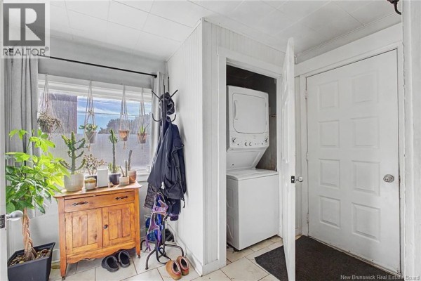 Interior entryway with a stacked washer and dryer, plants, and a wooden cabinet. - 2 River Street, Fredericton