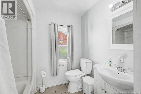 Small bathroom with a white bathtub, toilet, sink, and frosted window. - 2 River Street, Fredericton