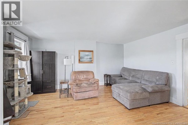 Living room with hardwood floors, a gray sectional sofa, armchair, and a tall dark wood cabinet. - 2 River Street, Fredericton