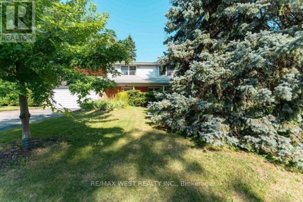 Front view of the house from the lawn, partially obscured by a large evergreen tree and deciduous trees. - 2 Robinter Drive, Toronto
