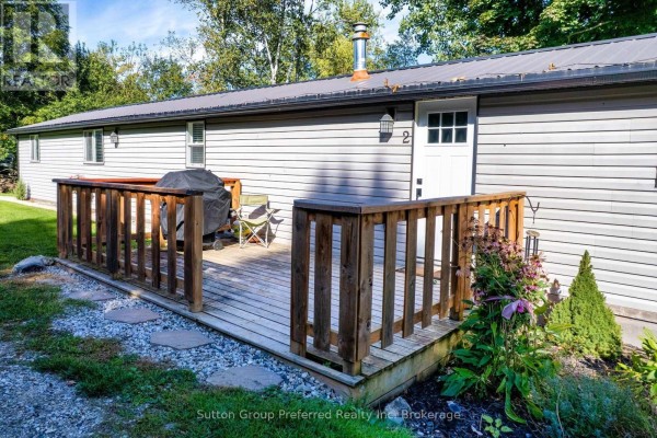 Wooden deck with railing attached to a grey mobile home, featuring a grill and a chair. - 2 Snowbird Lane - 596101 59 Highway, East Zorra Tavistock