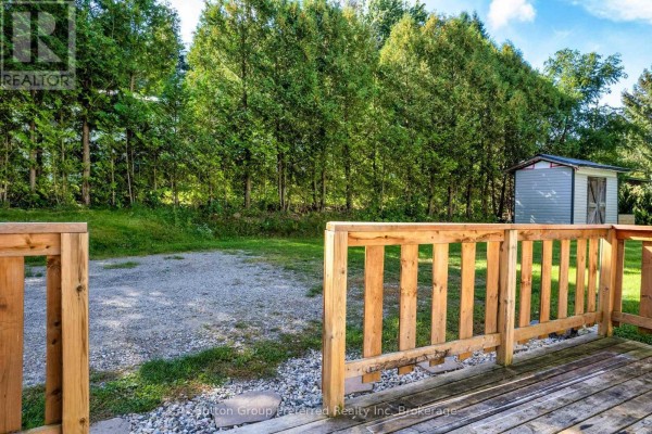 View from a wooden deck looking towards a gravel driveway and a small storage shed. - 2 Snowbird Lane - 596101 59 Highway, East Zorra Tavistock