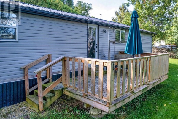 Close-up of the wooden deck with stairs, attached to the grey mobile home, with a large umbrella. - 2 Snowbird Lane - 596101 59 Highway, East Zorra Tavistock