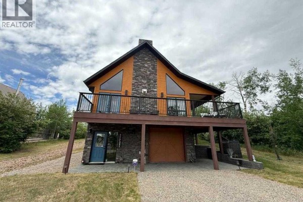 Front view of the house featuring stone accents, large deck, and driveway in a snowy landscape. - 2 Sunset Lane, Rural Stettler No  6, County Of