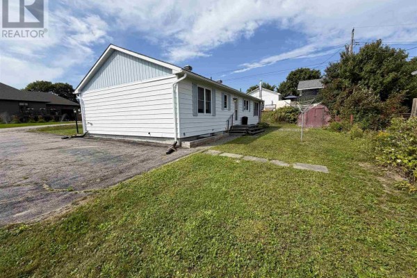View of the side and backyard of a bungalow with a paved driveway and grassy area. - 2 Tecumseh Rd, Elliot Lake
