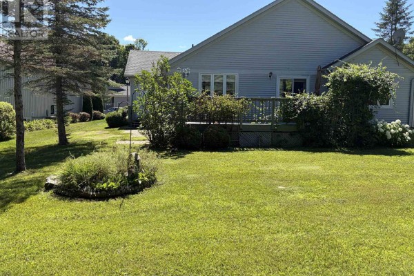 Backyard view with a wooden deck, lush green lawn, mature trees, and overgrown garden beds. - 2 Twigs End, Gravenhurst)