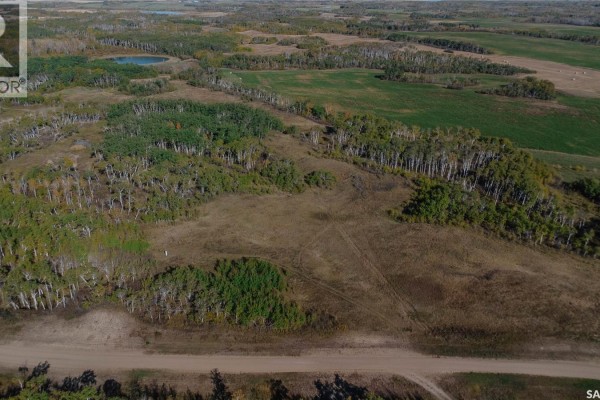Aerial view of rural land with scattered trees, a small pond, and agricultural fields under a blue sky. - 2 Whitetail Trail, Duck Lake Rm No  463