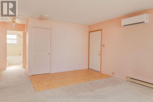 Interior view of a living room with light pink walls, beige carpet, and a large air conditioning unit. - 20 - 303 Waterloo Street, Saugeen Shores