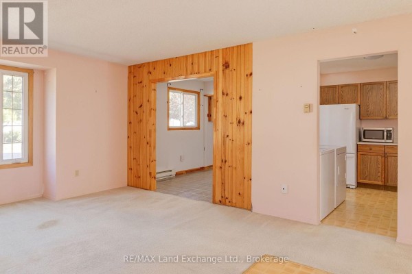 Interior view of a living room with light pink walls, beige carpet, and a doorway with wood paneling leading to another room. - 20 - 303 Waterloo Street, Saugeen Shores