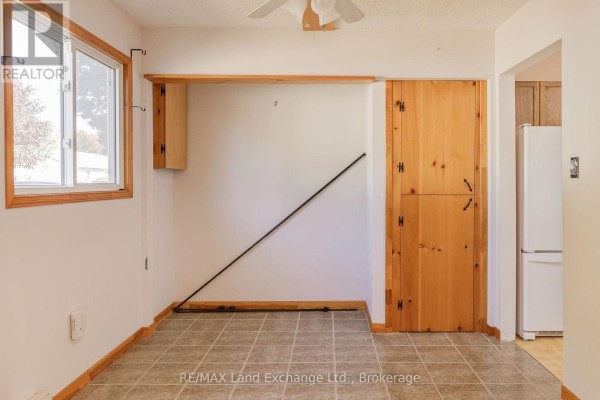 Interior view of a room with tiled flooring, white walls, a window, and a wooden door leading to the kitchen area. - 20 - 303 Waterloo Street, Saugeen Shores