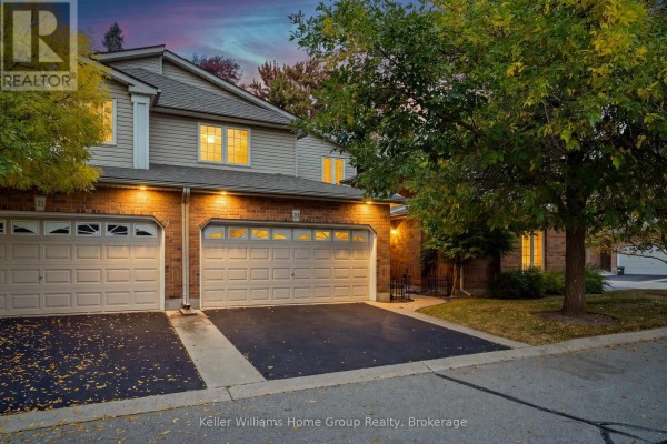 Exterior townhouse with brick and siding, two lit beige garage doors, and paved driveway at dusk. - 20 - 784 Gordon Street, Guelph