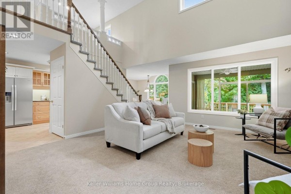 Living room with a white sofa, beige carpet, wood coffee tables, and large window with green view. - 20 - 784 Gordon Street, Guelph
