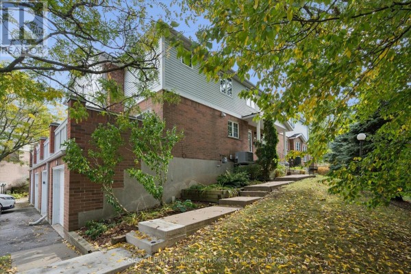 Side view of townhouse with red brick, white siding, and grass yard with fallen leaves. - 20 - 941 Gordon Street, Guelph