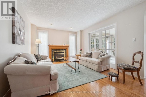 Living room with two beige sofas, wooden coffee table, fireplace, and French doors. - 20 - 941 Gordon Street, Guelph