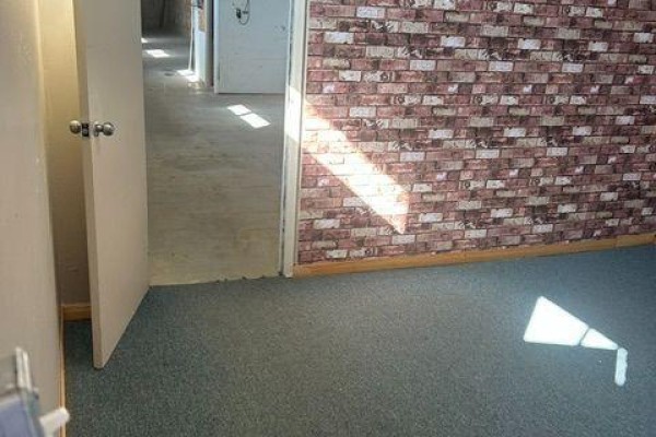 Interior view from a doorway into a room with blue carpet and a red brick accent wall. - 20 & 21 - 106 Saunders Road, Barrie