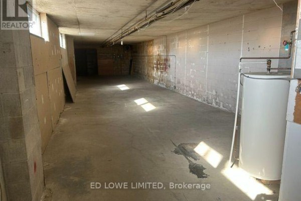 Unfinished basement interior with concrete floor and walls, water heater, and exposed pipes. - 20 & 21 - 106 Saunders Road, Barrie