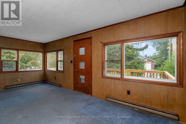 A room with blue carpet, wood-paneled walls, a wooden door, and large windows overlooking the exterior deck. - 20 61st Street S, Wasaga Beach