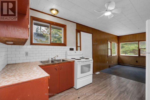 A kitchen area with a sink, stove, and cabinets, opening into a room with wood-paneled walls and windows. - 20 61st Street S, Wasaga Beach