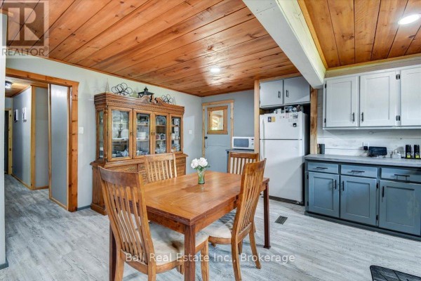 Dining area with a wooden table and chairs, facing a large china cabinet and an open doorway. - 20 Art Bott Road, North Kawartha