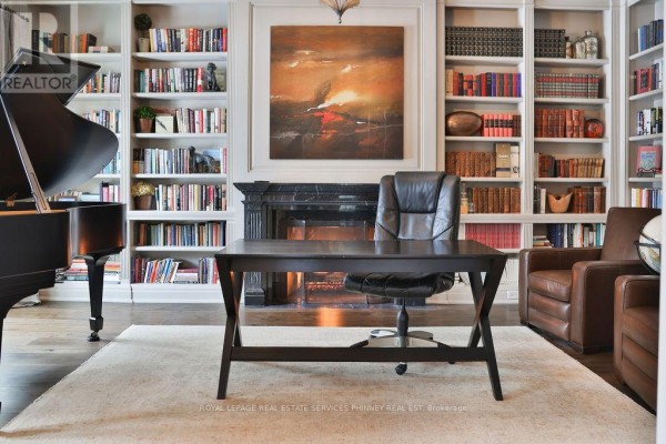 Library with floor-to-ceiling bookshelves, fireplace, piano, desk, and leather armchairs. - 20 Cluny Drive, Toronto