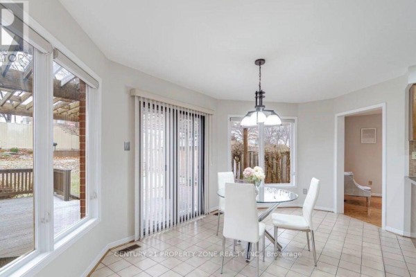 Breakfast nook with a round glass table, white chairs, and large windows overlooking the backyard. - 20 Corkett Drive, Brampton