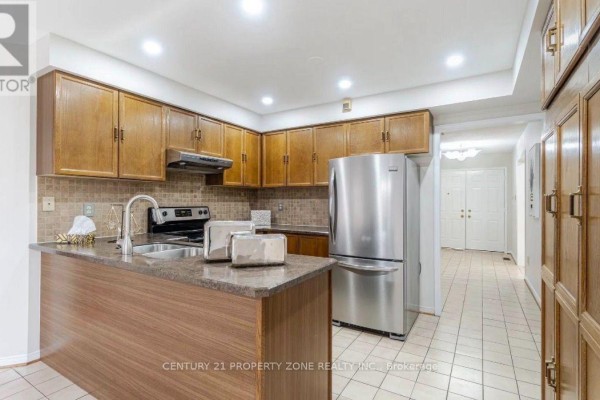 Kitchen with wood cabinets, granite countertops, a stainless steel refrigerator, and tile flooring. - 20 Corkett Drive, Brampton