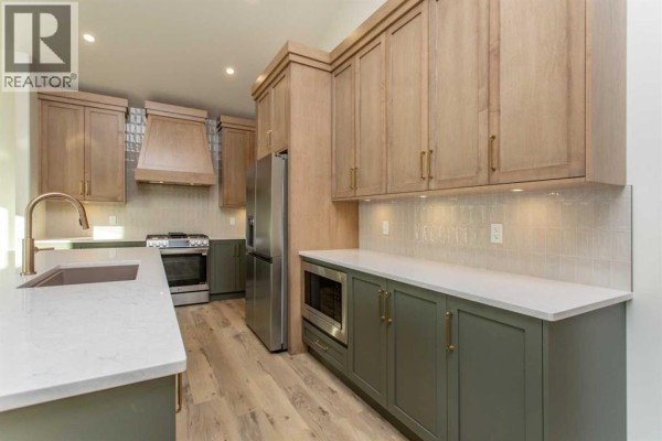 Modern kitchen with light wood cabinetry, grey lower cabinets, stainless steel appliances, and white countertops. - 20 Emmett Crescent, Red Deer