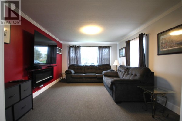 Living room with gray carpet, dark gray sofas, and red accent wall. - 20 Evergreen Drive, Paradise